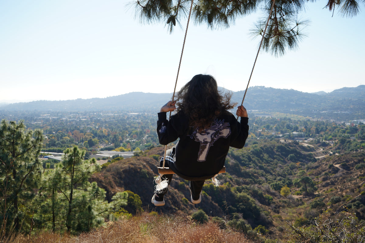 Back of the Always Prosper Trinity crewneck worn on a rope swing over a canyon