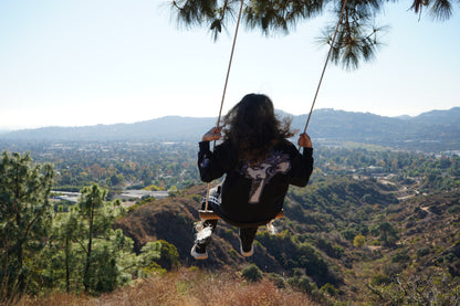 Back of the Always Prosper Trinity crewneck worn on a rope swing over a canyon