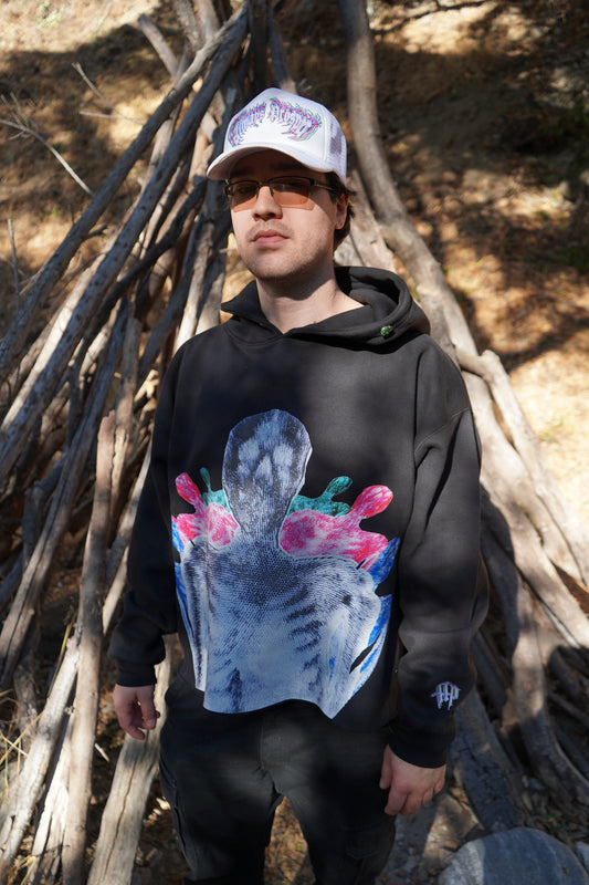 Model wearing the Always Prosper Skelly black hoodie with its blue and pink sacred heart print