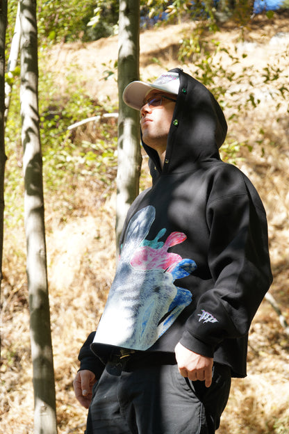The Skelly black hoodie worn with the hood up, sacred heart print across the chest