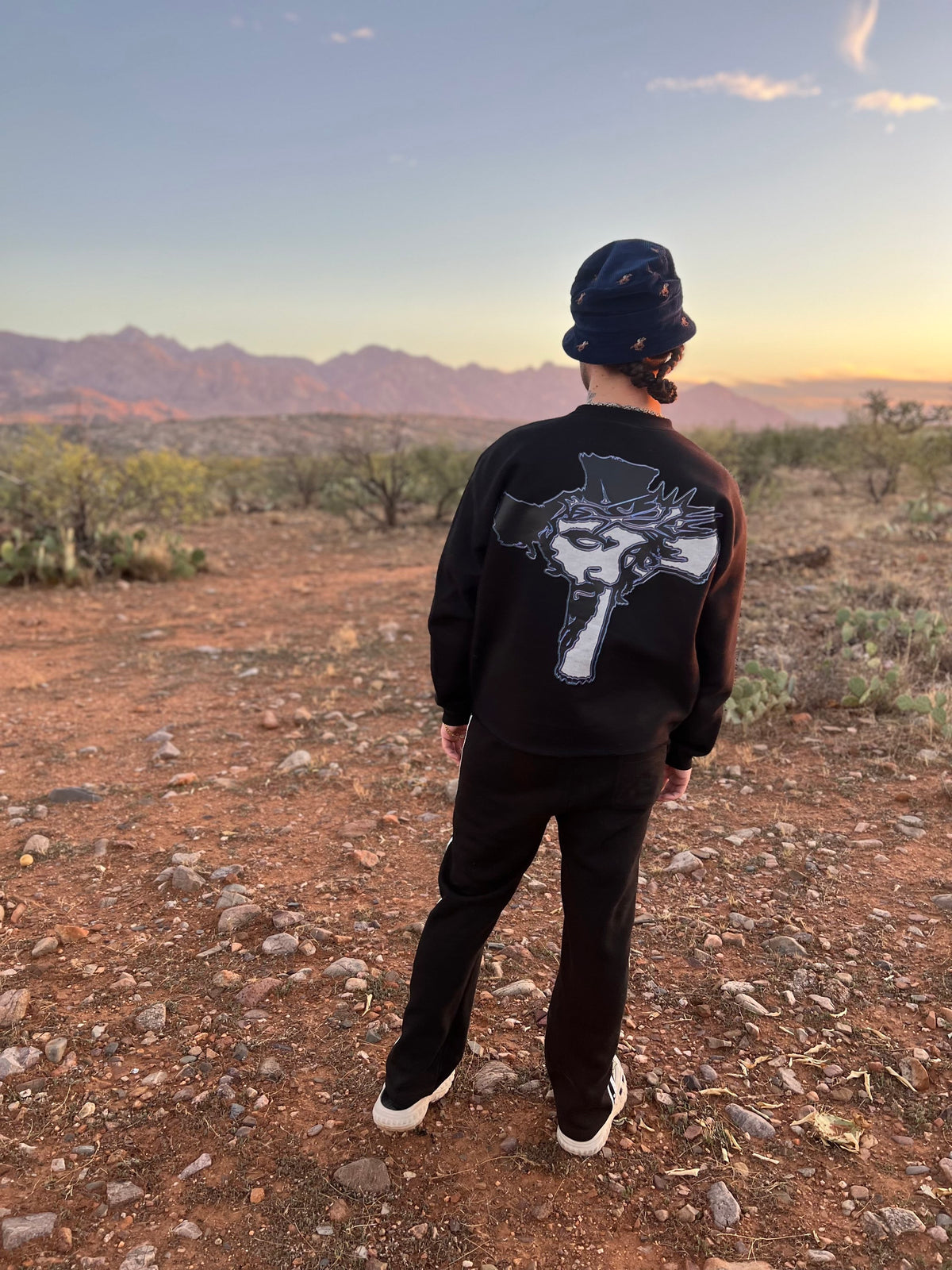 Cross graphic on the back of the Always Prosper Trinity crewneck, worn in the desert at sunset