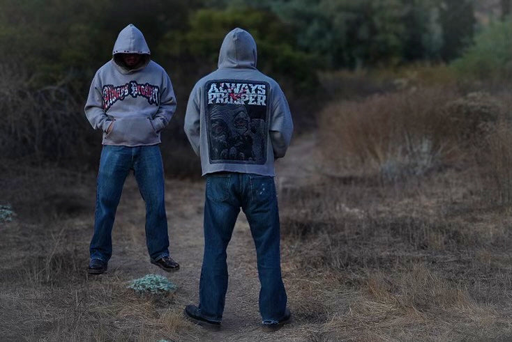 Two models wearing the Always Prosper Scream stone grey hoodie outdoors at dusk, front and back