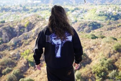 Large cross graphic across the back of the Trinity crewneck, worn on a hillside above the valley